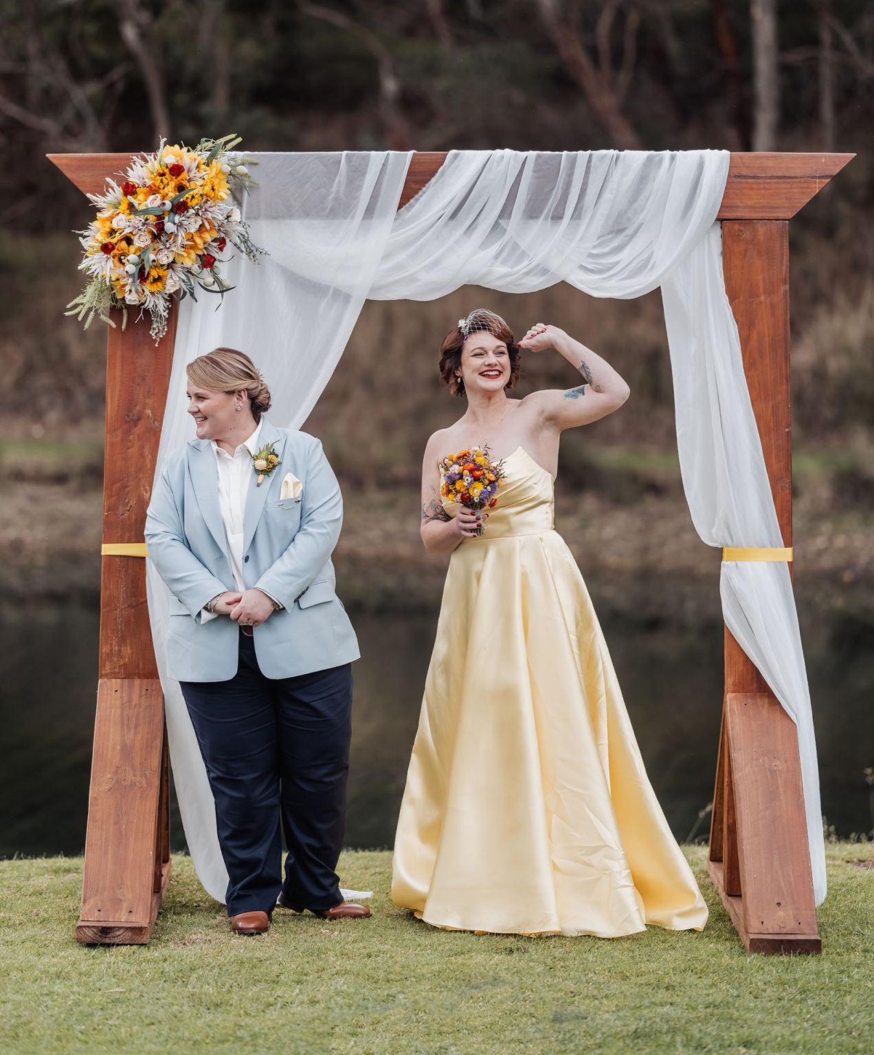 tiny house on the prairie wedding - lauren & bek 20 Outdoor wedding couple beneath rustic wooden arch with white drapery and colorful flowers.