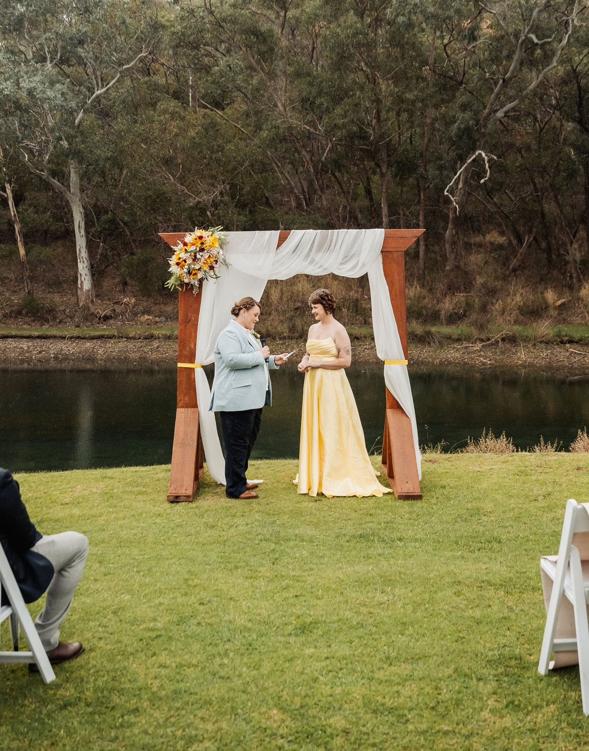 tiny house on the prairie wedding - lauren & bek 30 Outdoor wedding ceremony by lake with wooden arch, floral decor, and couple exchanging vows.
