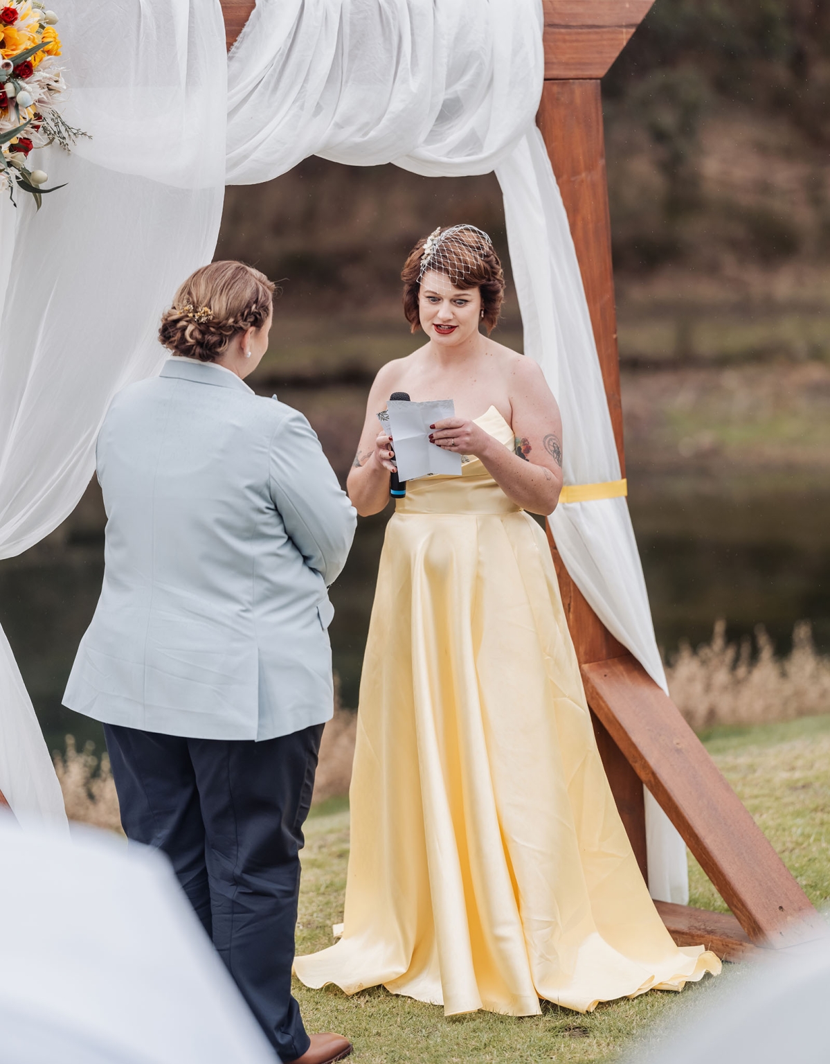 tiny house on the prairie wedding - lauren & bek 29 Outdoor wedding vows under a white draped arch with romantic floral ceremony decor.