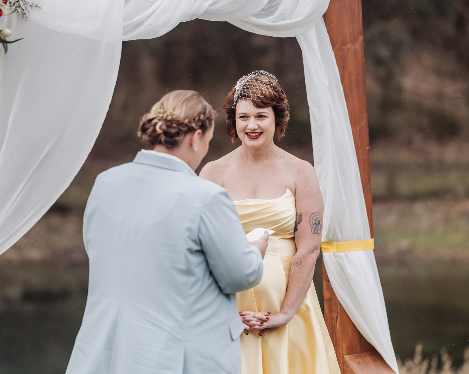 tiny house on the prairie wedding - lauren & bek 27 Outdoor wedding vows under wooden arch with smiling bride in pale yellow gown.