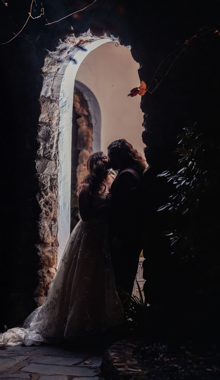 basket range wedding at the manor - leah & wes 64 Romantic wedding couple kissing under rustic stone archway in dramatic backlight.