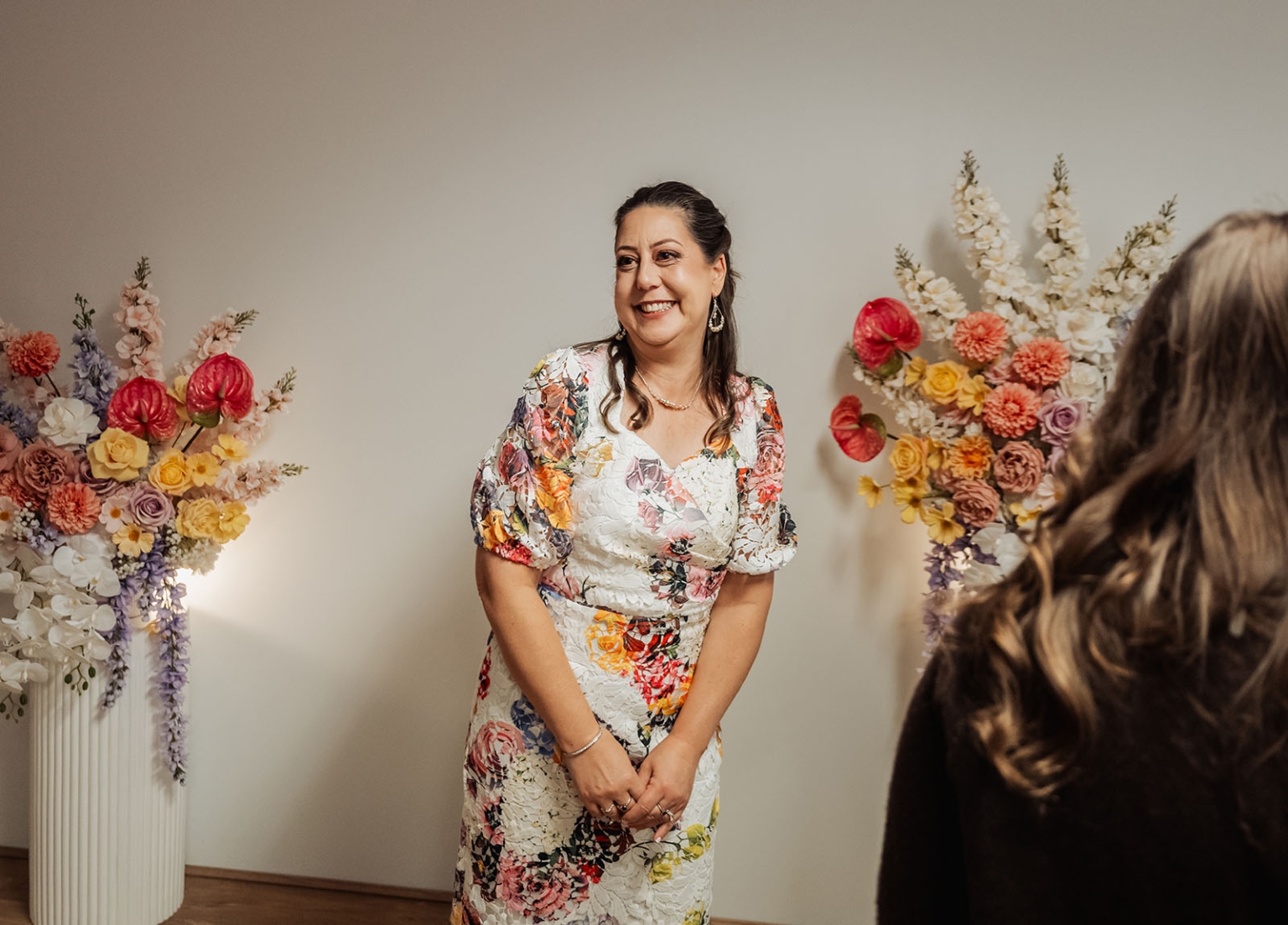 sa marriage office wedding – melissa & kyran 204 Smiling woman in floral dress at elegant indoor party with pastel flower arrangements.