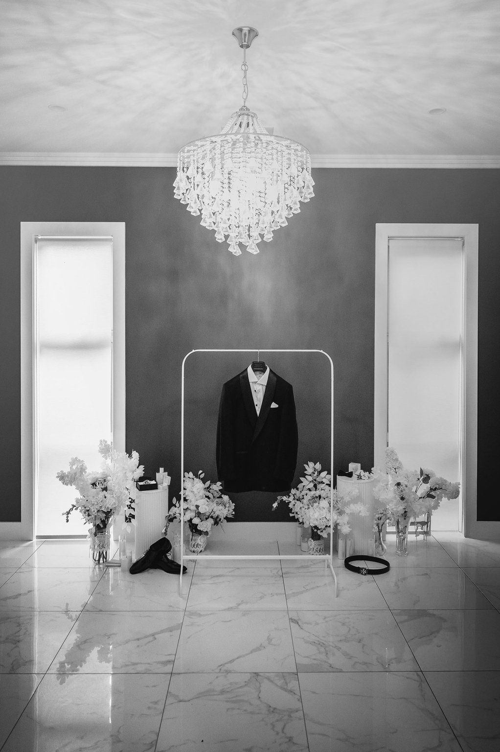 st george & st shenouda coptic church wedding - carmina & bill 1 Elegant wedding tuxedo on rack beneath crystal chandelier in luxury bridal suite.