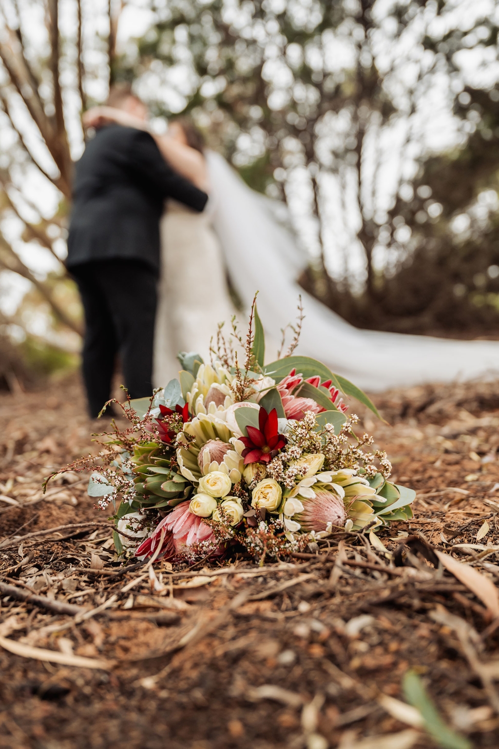 loxton's st peter's church wedding - madeline & brayden 55 Wedding bouquet on forest floor with bride and groom blurred among trees.