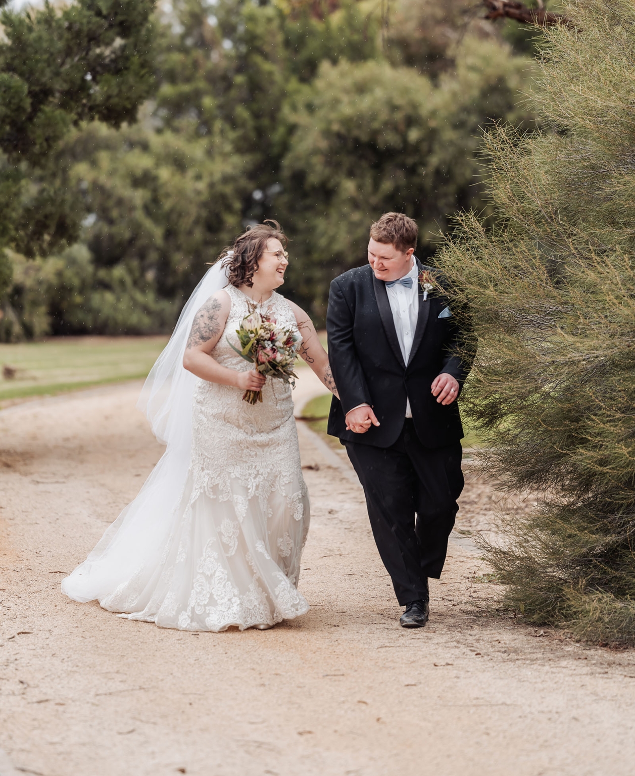 loxton's st peter's church wedding - madeline & brayden 48 Joyful wedding couple holding hands on garden path in romantic outdoor portrait.