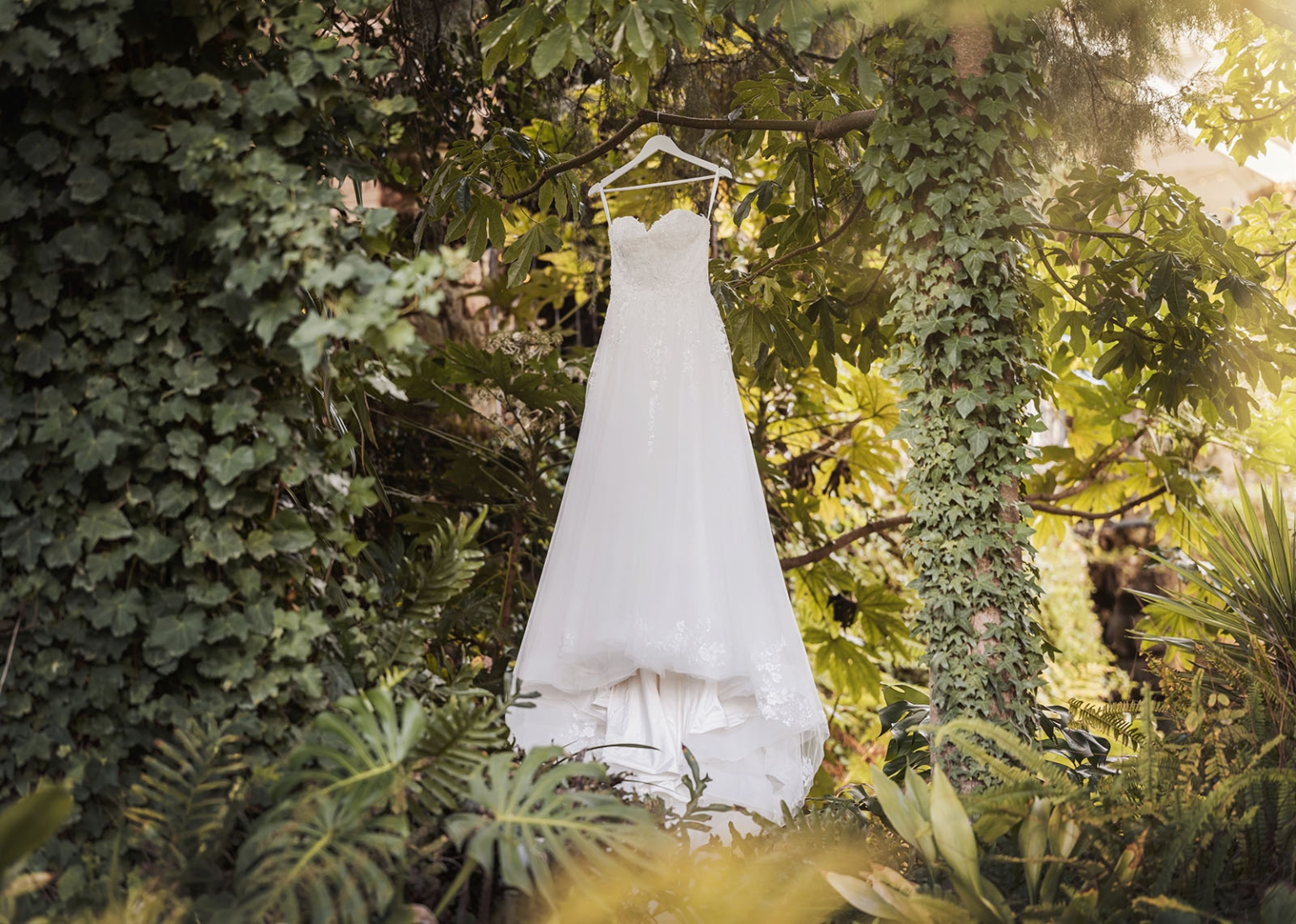the manor wedding - crystal & mackenzie 13 White wedding dress hanging in lush garden with lace bridal gown details.