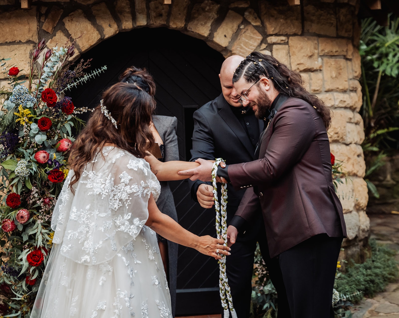 basket range wedding at the manor - leah & wes 51 Wedding handfasting ceremony under a rustic stone arch with lush floral arrangements.