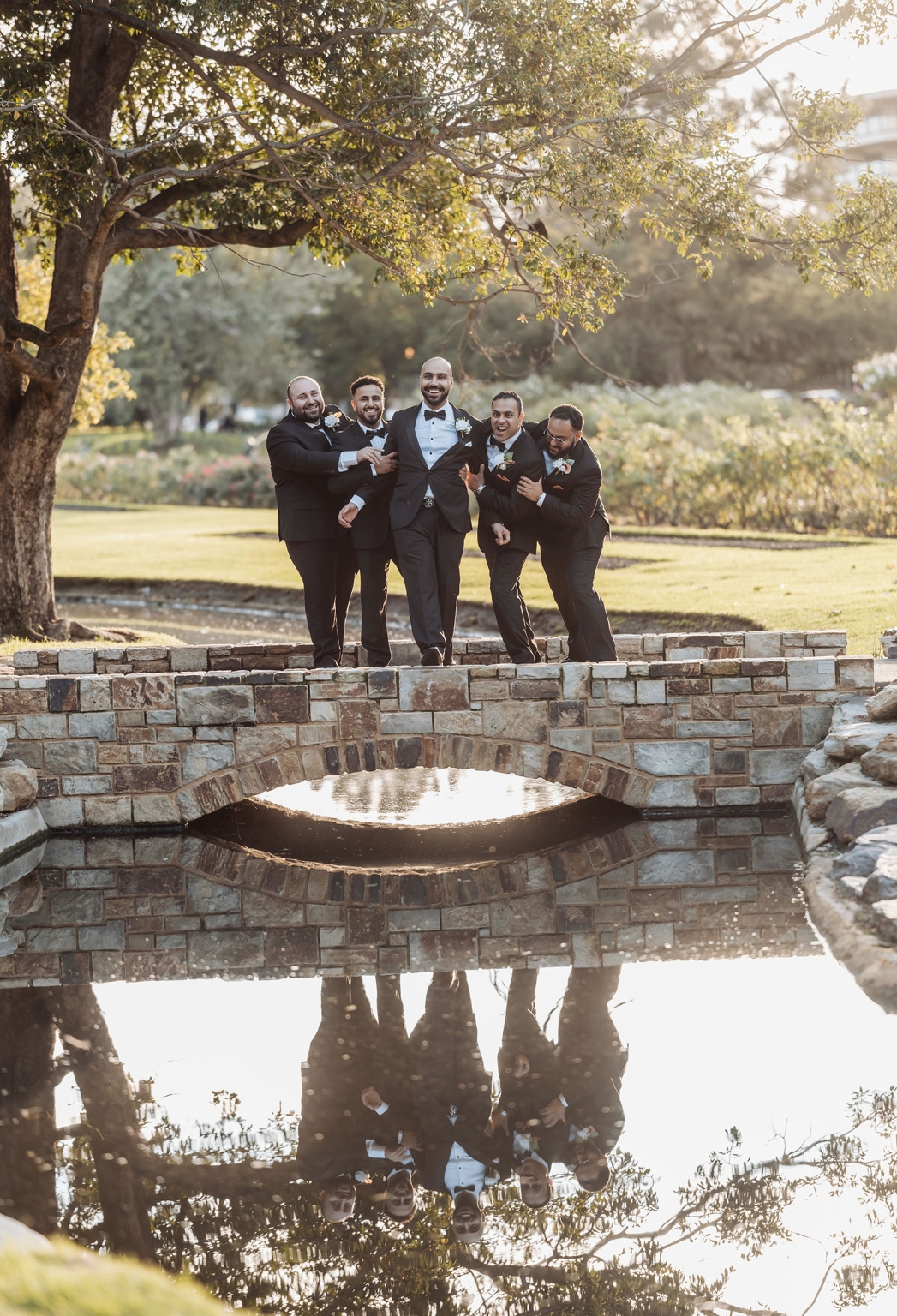 st george & st shenouda coptic church wedding - carmina & bill 64 Groom and groomsmen in tuxedos on stone bridge at garden wedding.
