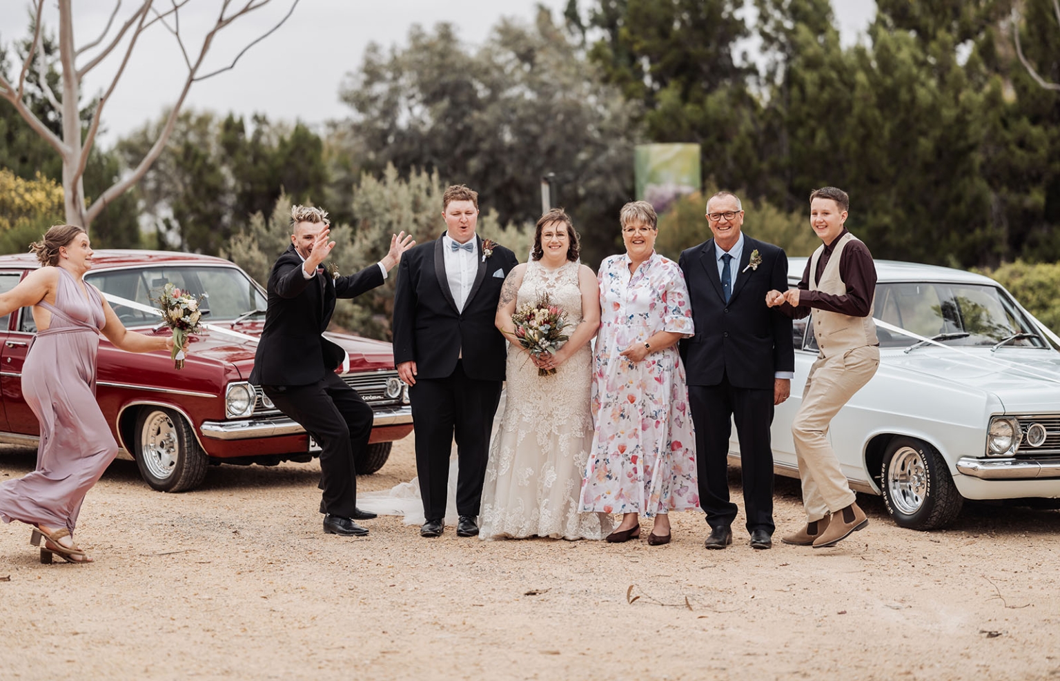 loxton's st peter's church wedding - madeline & brayden 44 Joyful wedding party posing with bride, groom, and vintage cars outdoors.