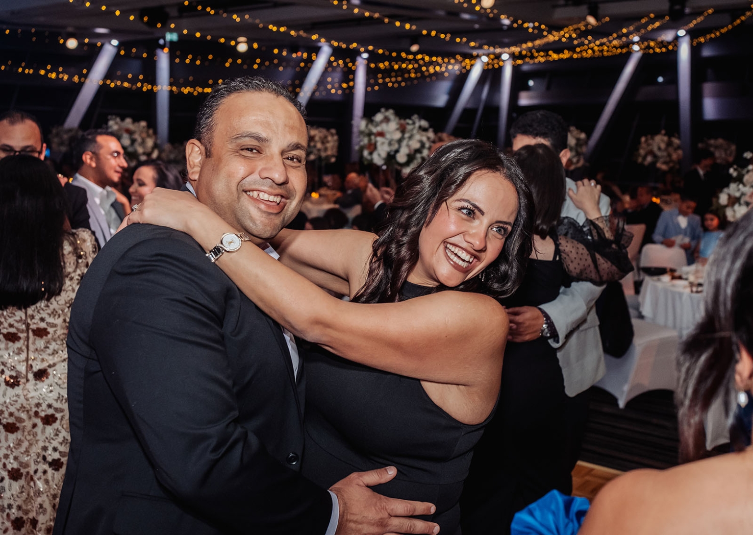 st george & st shenouda coptic church wedding - carmina & bill 87 Joyful couple dancing at a wedding reception under warm string lights.