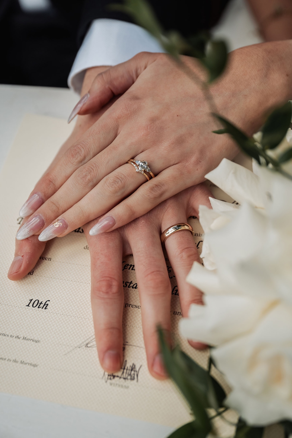 the manor wedding - crystal & mackenzie 58 Wedding rings on newlyweds’ hands over marriage certificate with white flowers.