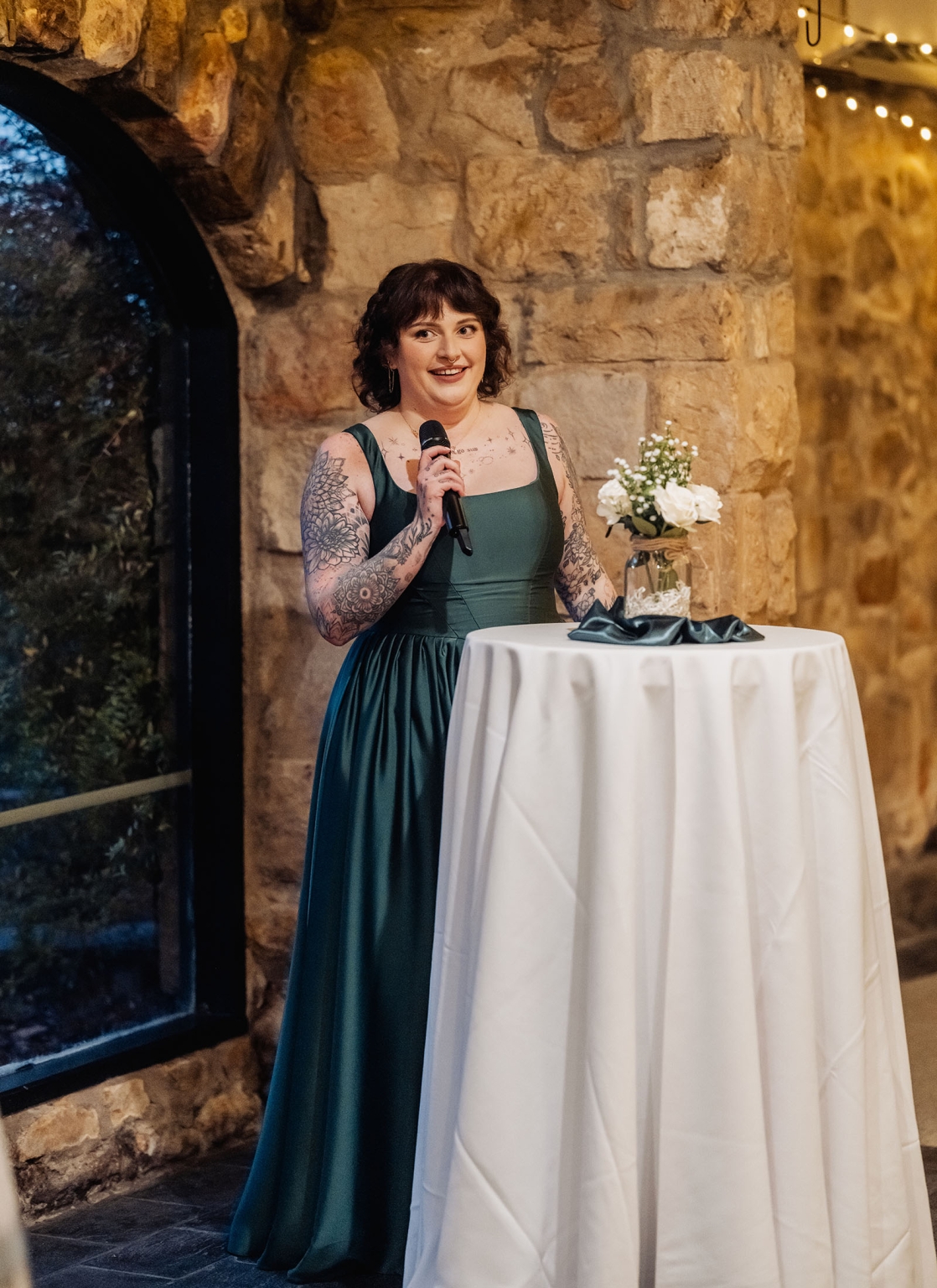 the manor wedding - crystal & mackenzie 89 Woman gives wedding toast in emerald dress at rustic stone reception venue.
