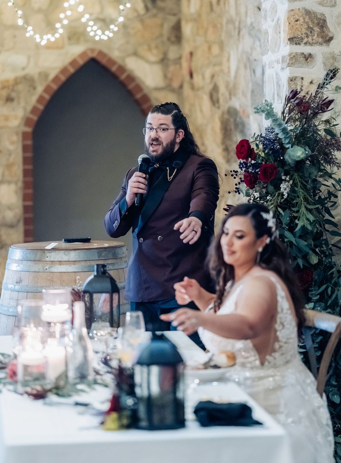 basket range wedding at the manor - leah & wes 74 Wedding toast in rustic stone venue with bride, string lights, and floral décor.