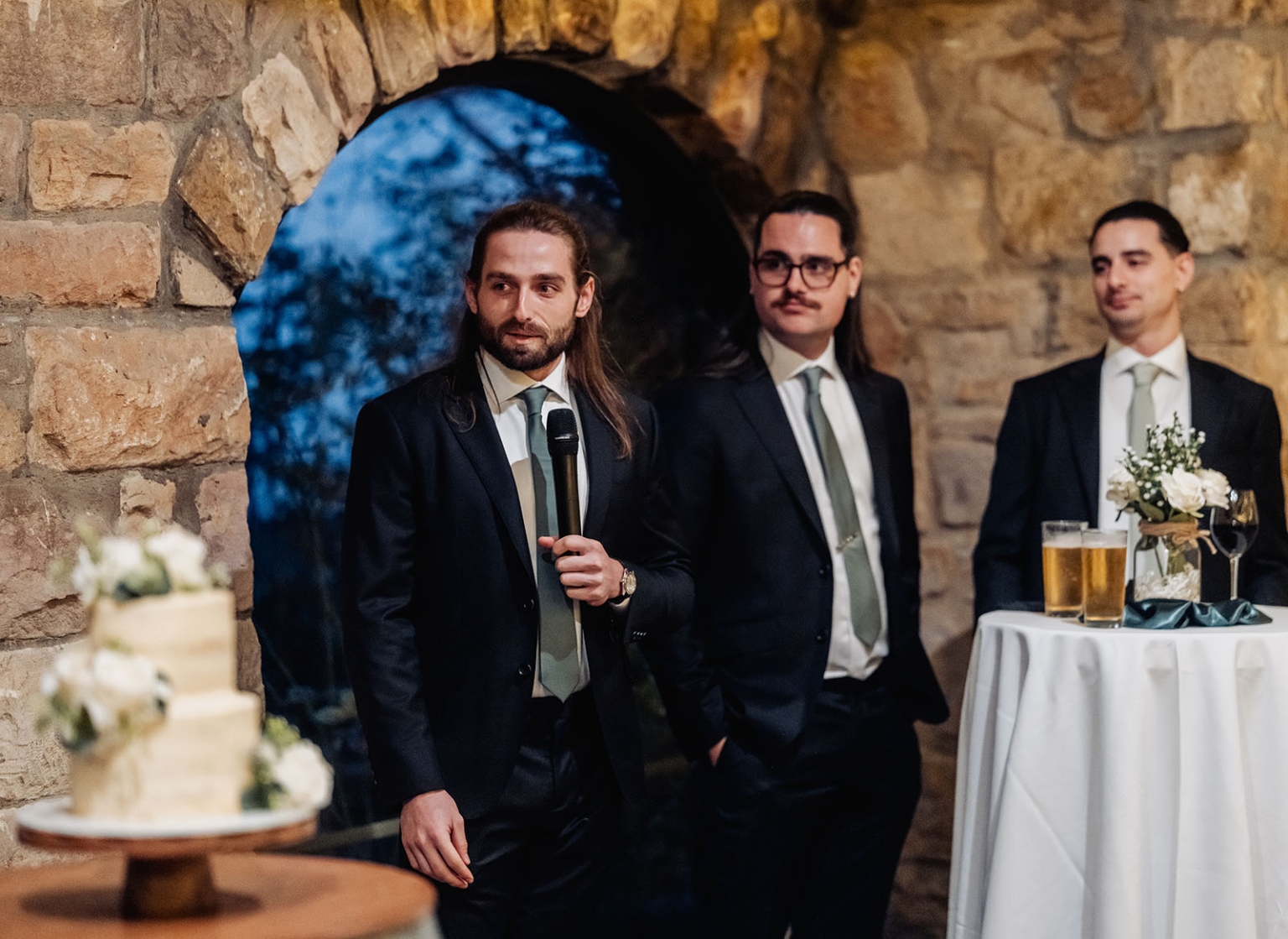 the manor wedding - crystal & mackenzie 90 Groomsmen wedding toast in rustic stone venue beside cake and floral cocktail table.