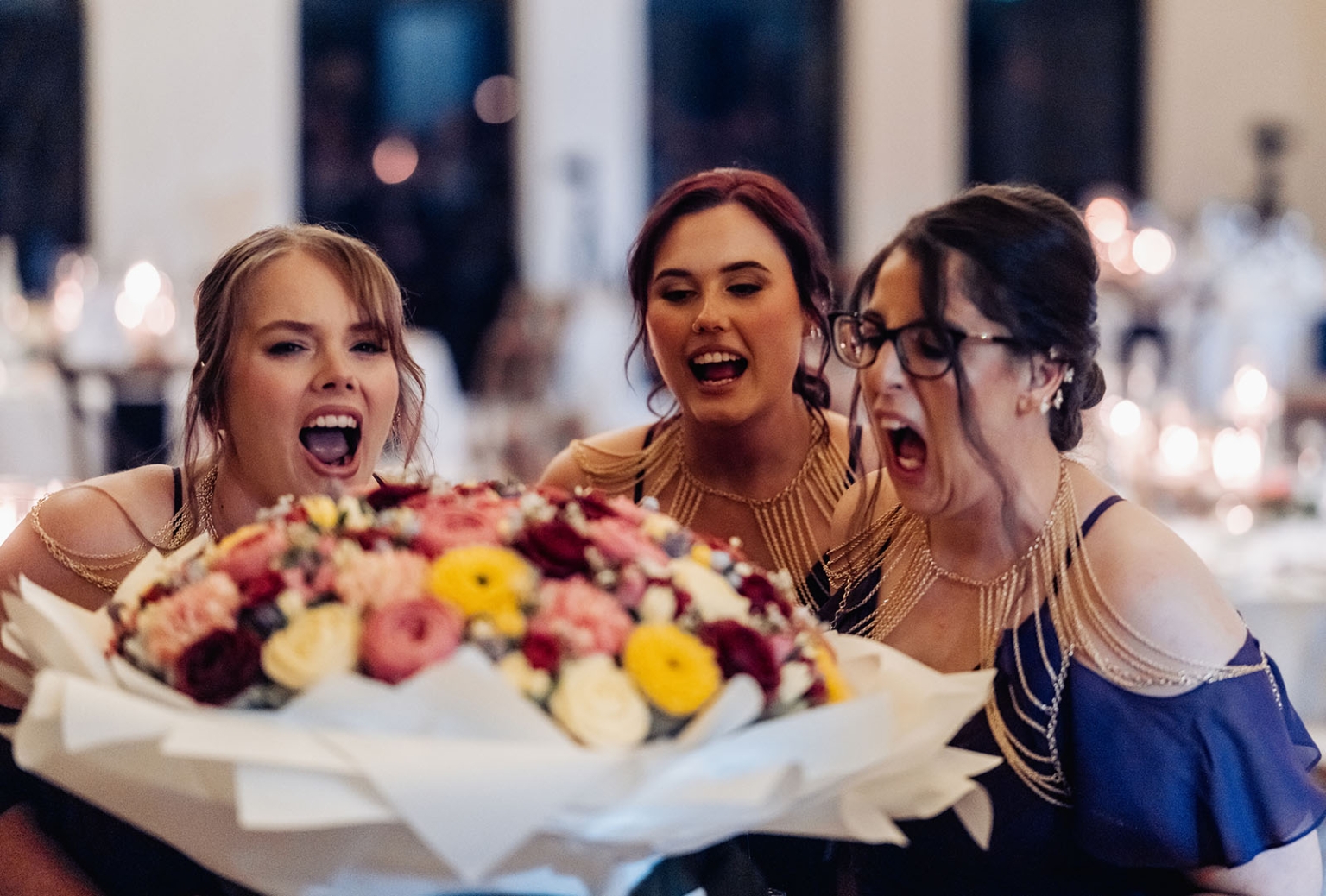 basket range wedding at the manor - leah & wes 69 Elegant women cheering behind a colorful wedding bouquet at a formal celebration.