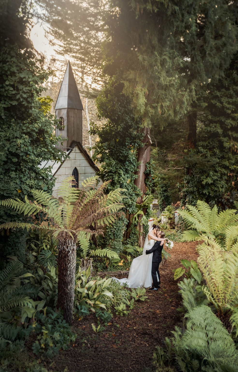 the manor wedding - crystal & mackenzie 64 Woodland wedding couple kissing on forest path beside ivy-covered chapel.