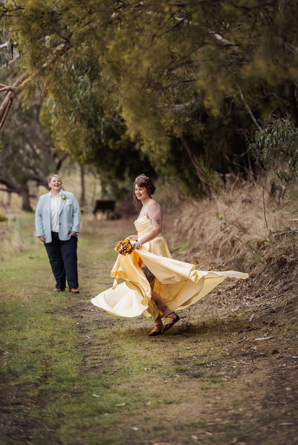 tiny house on the prairie wedding - lauren & bek 50 Bride twirling in yellow wedding dress on rustic woodland path with bouquet.