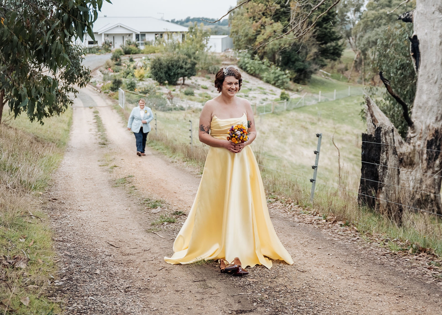 tiny house on the prairie wedding - lauren & bek 12 Bride in yellow gown holding bouquet on rustic countryside wedding road.