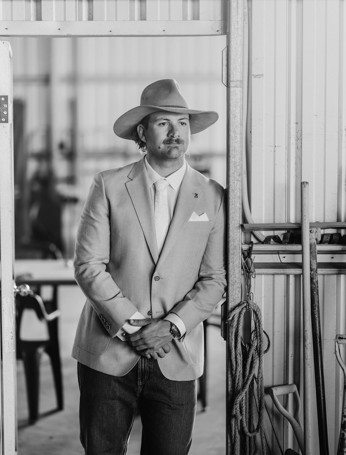 capella wedding photography – caitlin & adam’s farm wedding 117 Adam wearing a suit, tie and cowboy hat in a farm shed doorway