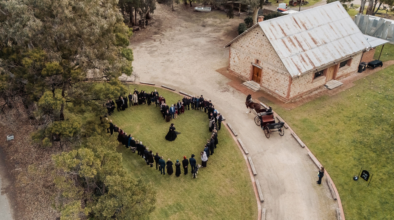 kuitpo hall wedding - courtney & jarrod 233 Aerial rural wedding guests form heart near historic stone barn and horse-drawn carriage.