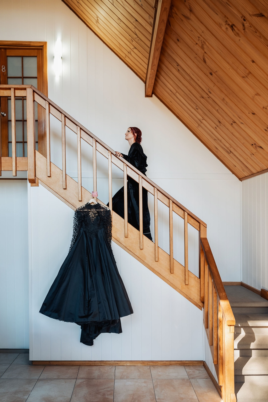 kuitpo hall wedding - courtney & jarrod 201 Black formal dress hanging on rustic wooden staircase with woman ascending.