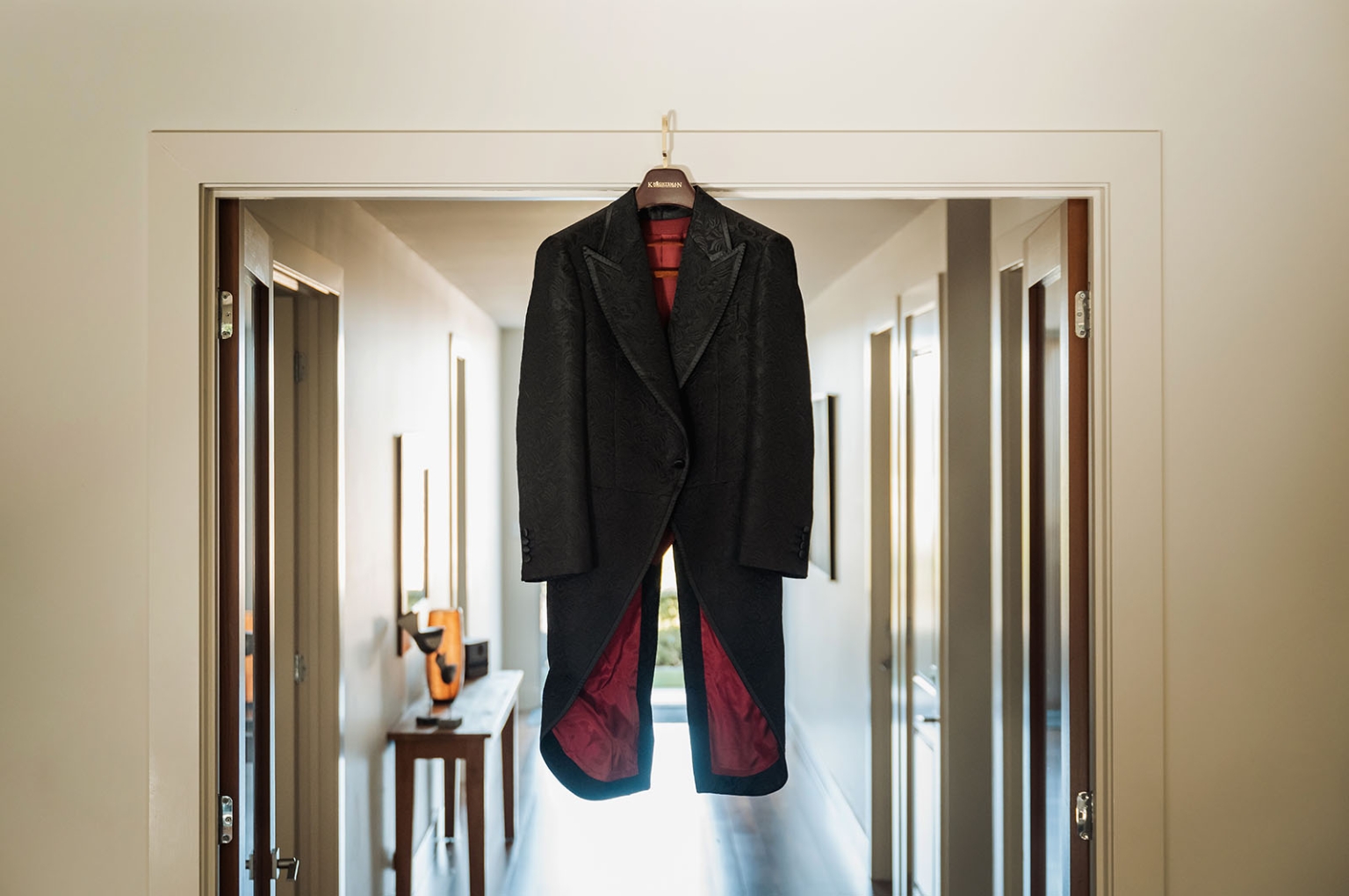 kuitpo hall wedding - courtney & jarrod 192 Black formal tailcoat with red lining hanging in elegant hallway doorway.