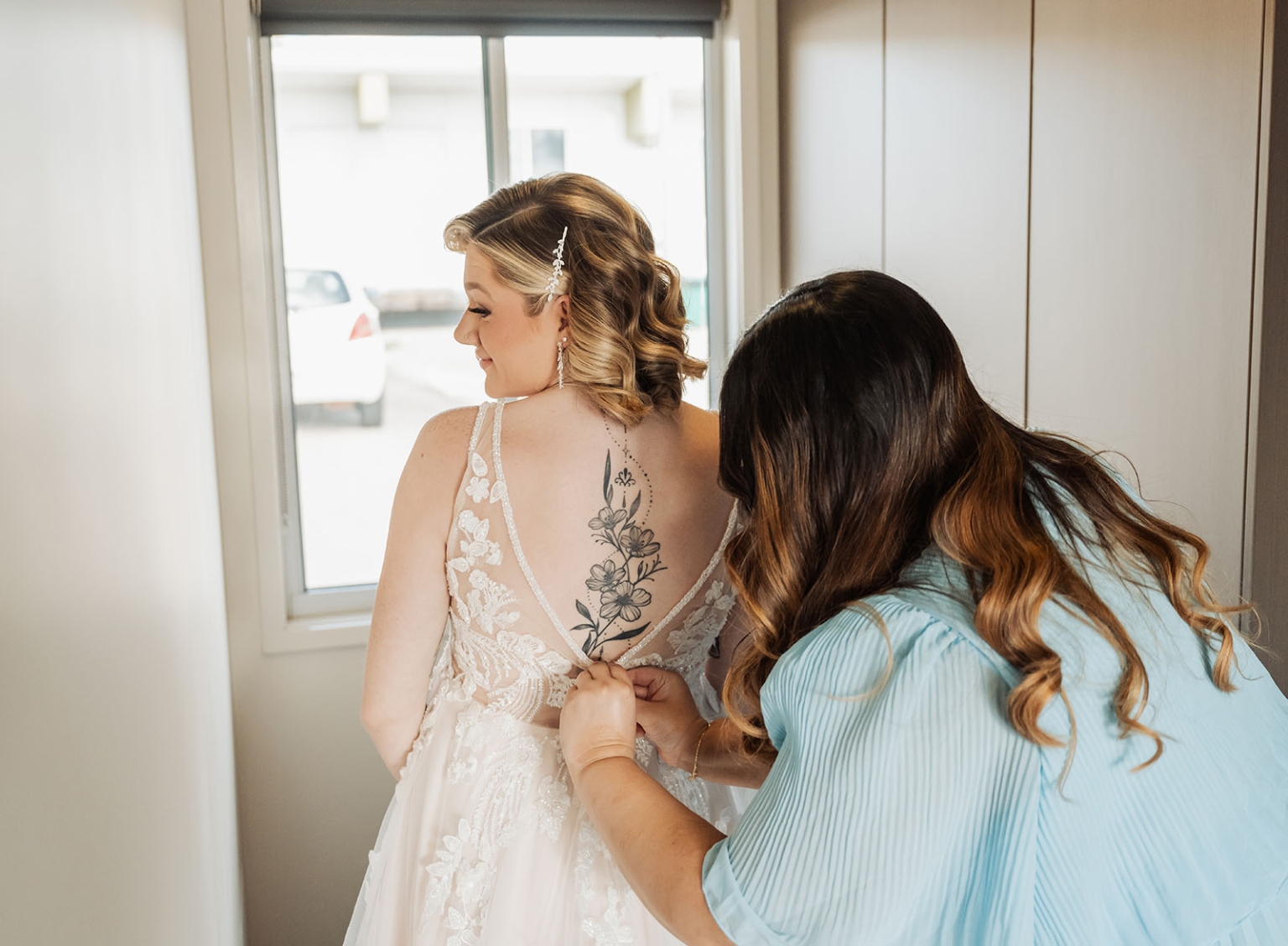 capella wedding photography – caitlin & adam’s farm wedding 126 Bride in a lace wedding dress as a woman fastens the open back, revealing a floral back tattoo
