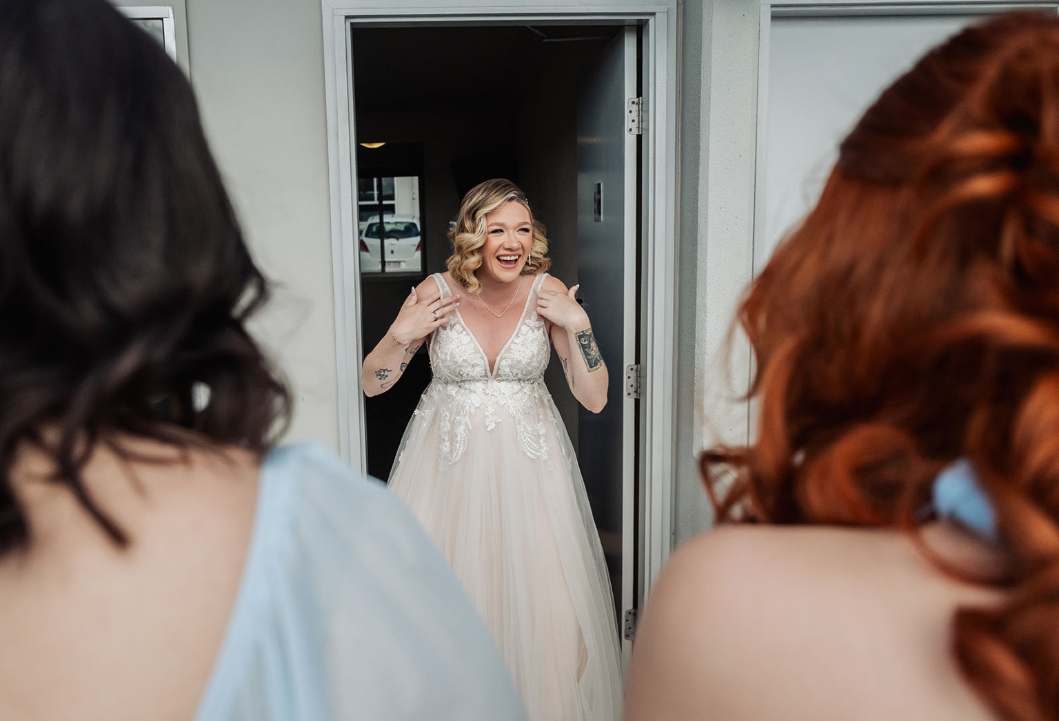 capella wedding photography – caitlin & adam’s farm wedding 131 Bride in a lace wedding dress laughing in a doorway as her bridesmaids look on