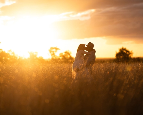 Caitlin and Adam embracing in a grassy field at sunset during their Capella farm wedding