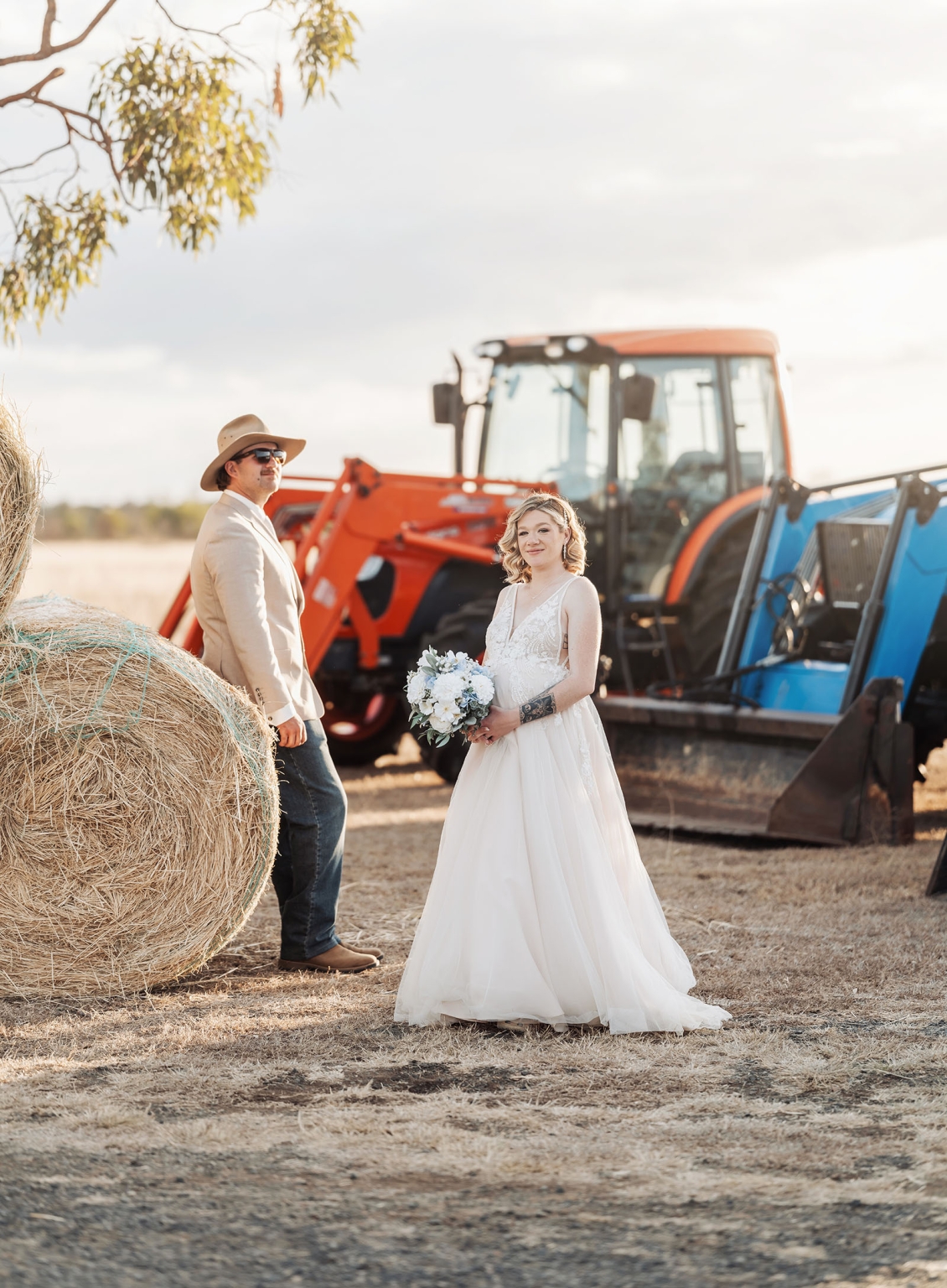 capella wedding photography – caitlin & adam’s farm wedding 161 Caitlin and Adam standing beside hay bales and tractors at their Capella farm wedding