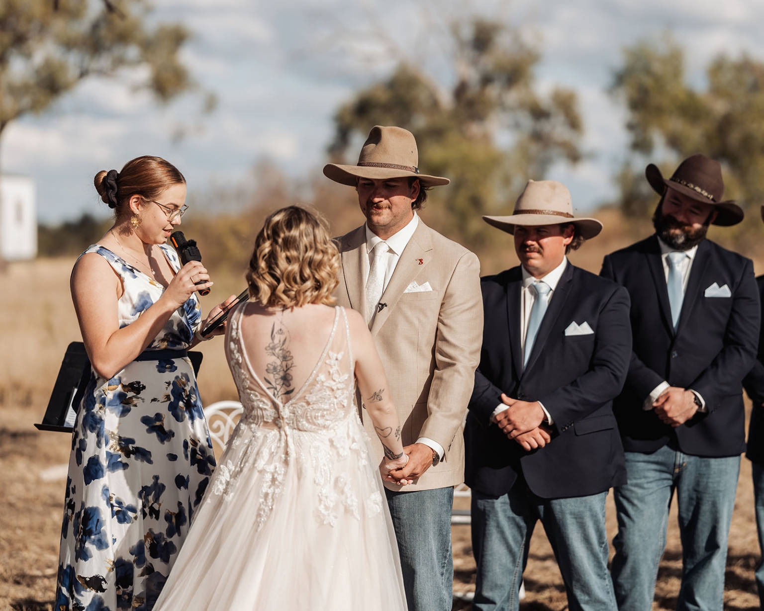 capella wedding photography – caitlin & adam’s farm wedding 140 Caitlin and Adam holding hands during their outdoor farm wedding ceremony, with the celebrant and groomsmen behind them.