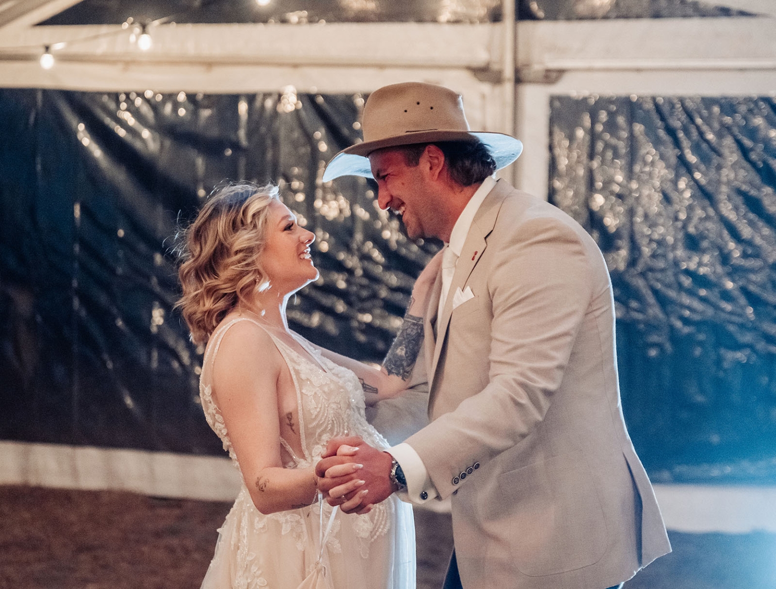 capella wedding photography – caitlin & adam’s farm wedding 176 Bride and groom smiling as they dance together beneath string lights at their Capella farm wedding