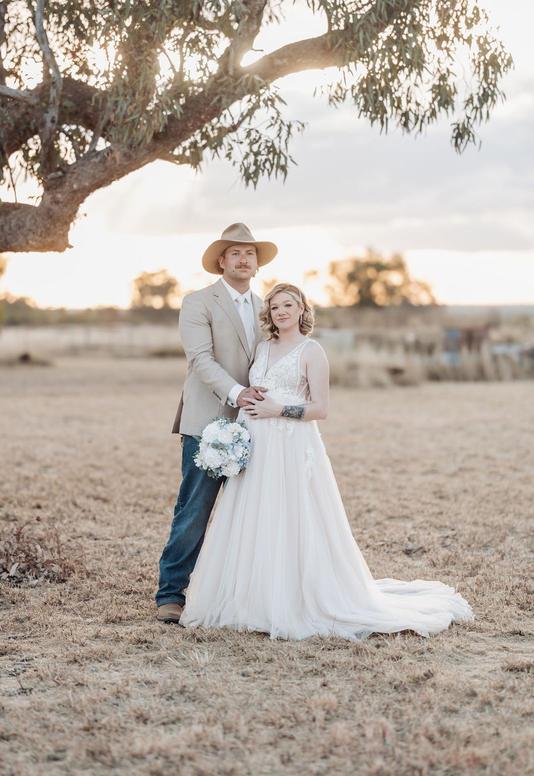 capella wedding photography – caitlin & adam’s farm wedding 167 Caitlin and Adam standing together beneath a large tree at their farm wedding in Capella, Queensland