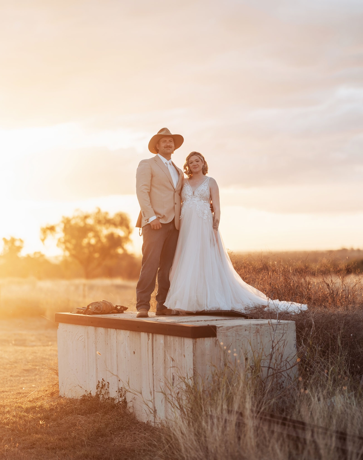 capella wedding photography – caitlin & adam’s farm wedding 172 Caitlin and Adam standing on a water tank in a grassy paddock at sunset, with Adam wearing a hat and Caitlin in a white wedding dress