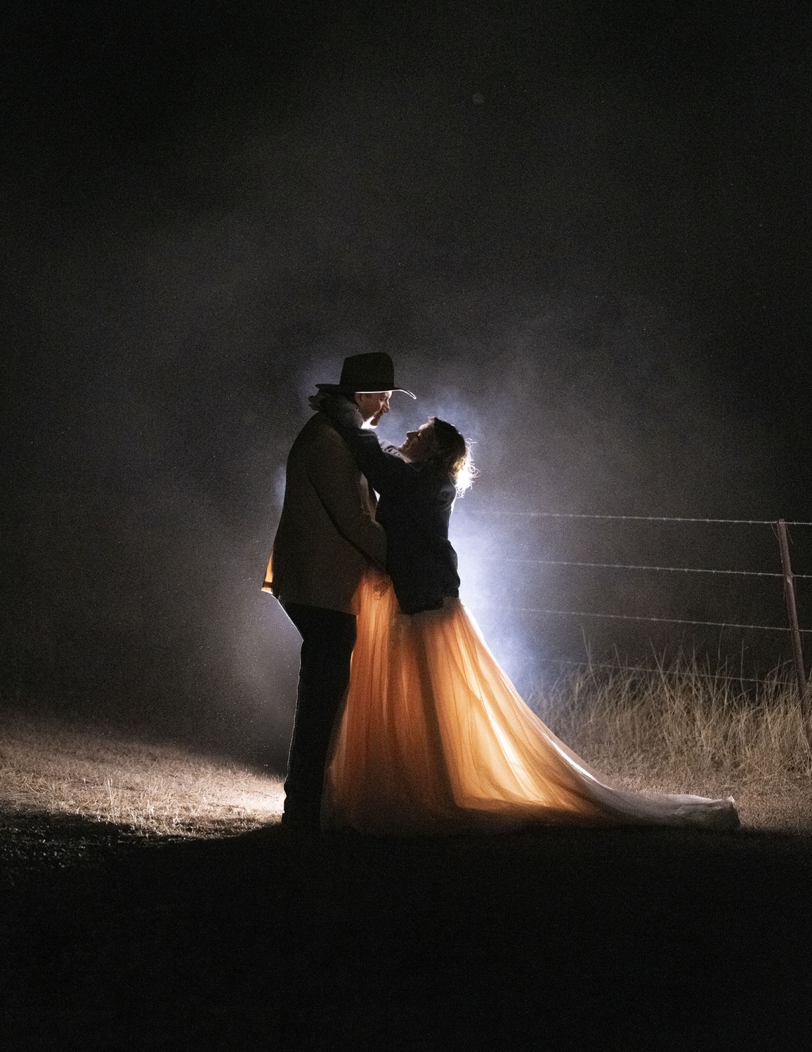 capella wedding photography – caitlin & adam’s farm wedding 188 Caitlin and Adam embracing outdoors at night, backlit by mist beside a farm fence in Capella