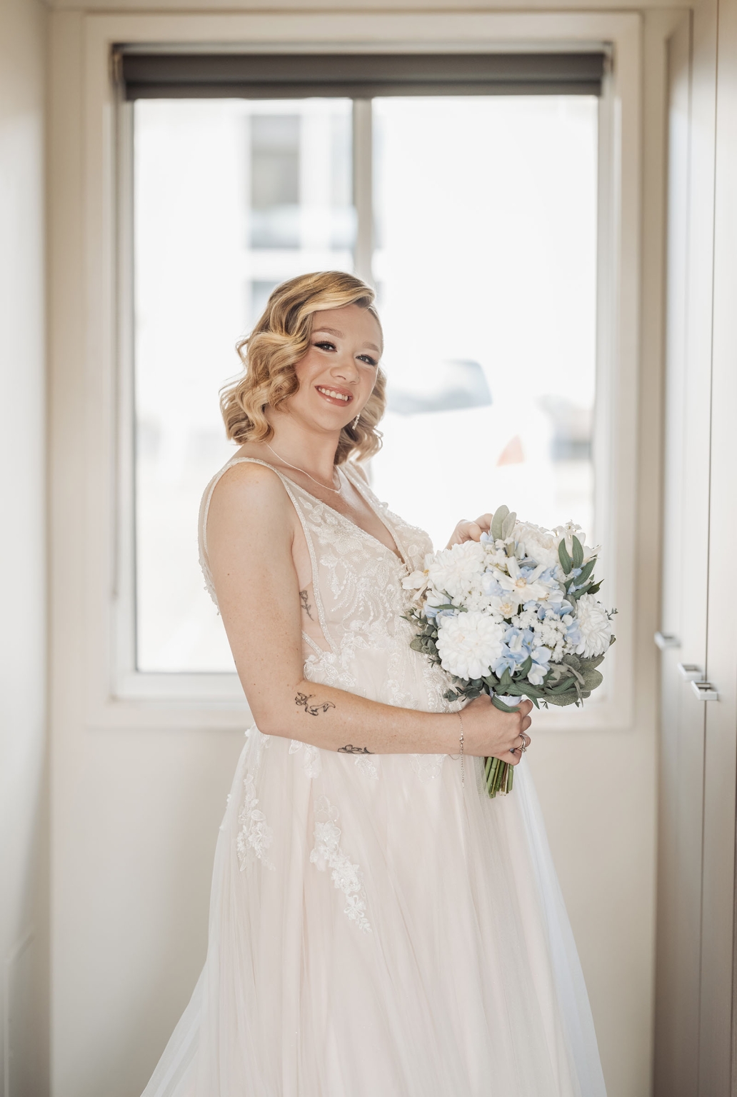 capella wedding photography – caitlin & adam’s farm wedding 127 Caitlin in her wedding dress holding a white and pale blue bouquet by a window