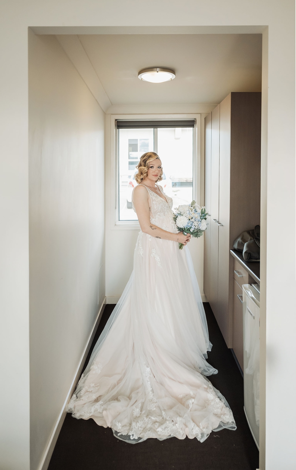 capella wedding photography – caitlin & adam’s farm wedding 128 Bride Caitlin in a lace wedding dress holding a white and pale blue bouquet beside a window