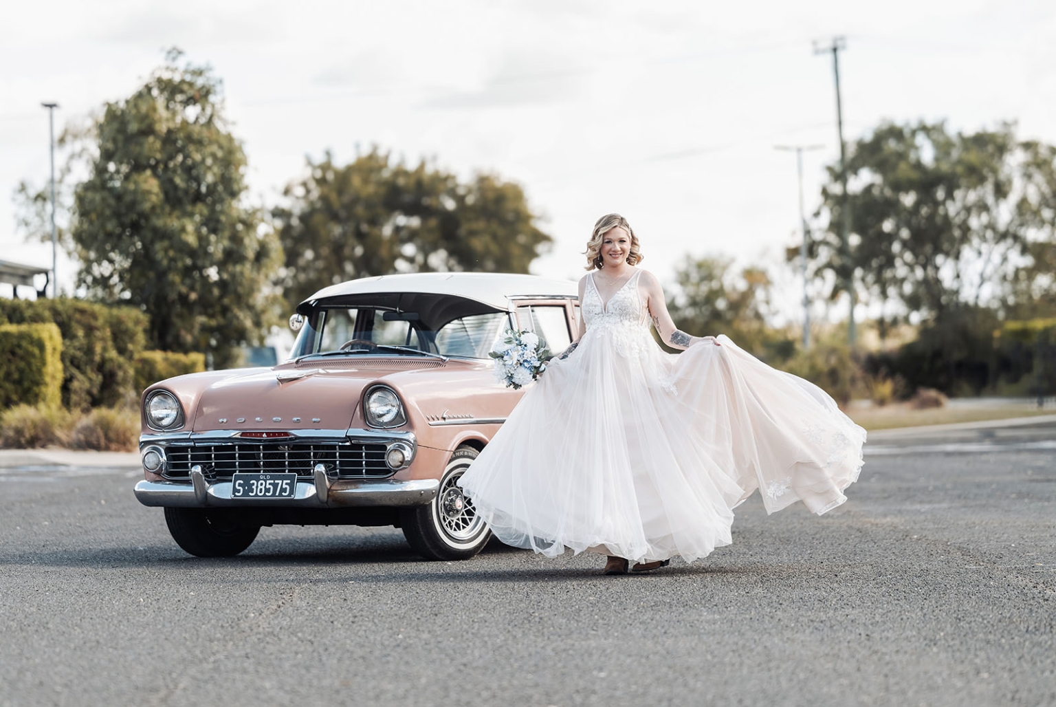 capella wedding photography – caitlin & adam’s farm wedding 132 Bride Caitlin holding her wedding dress beside a pink vintage Holden car in Capella
