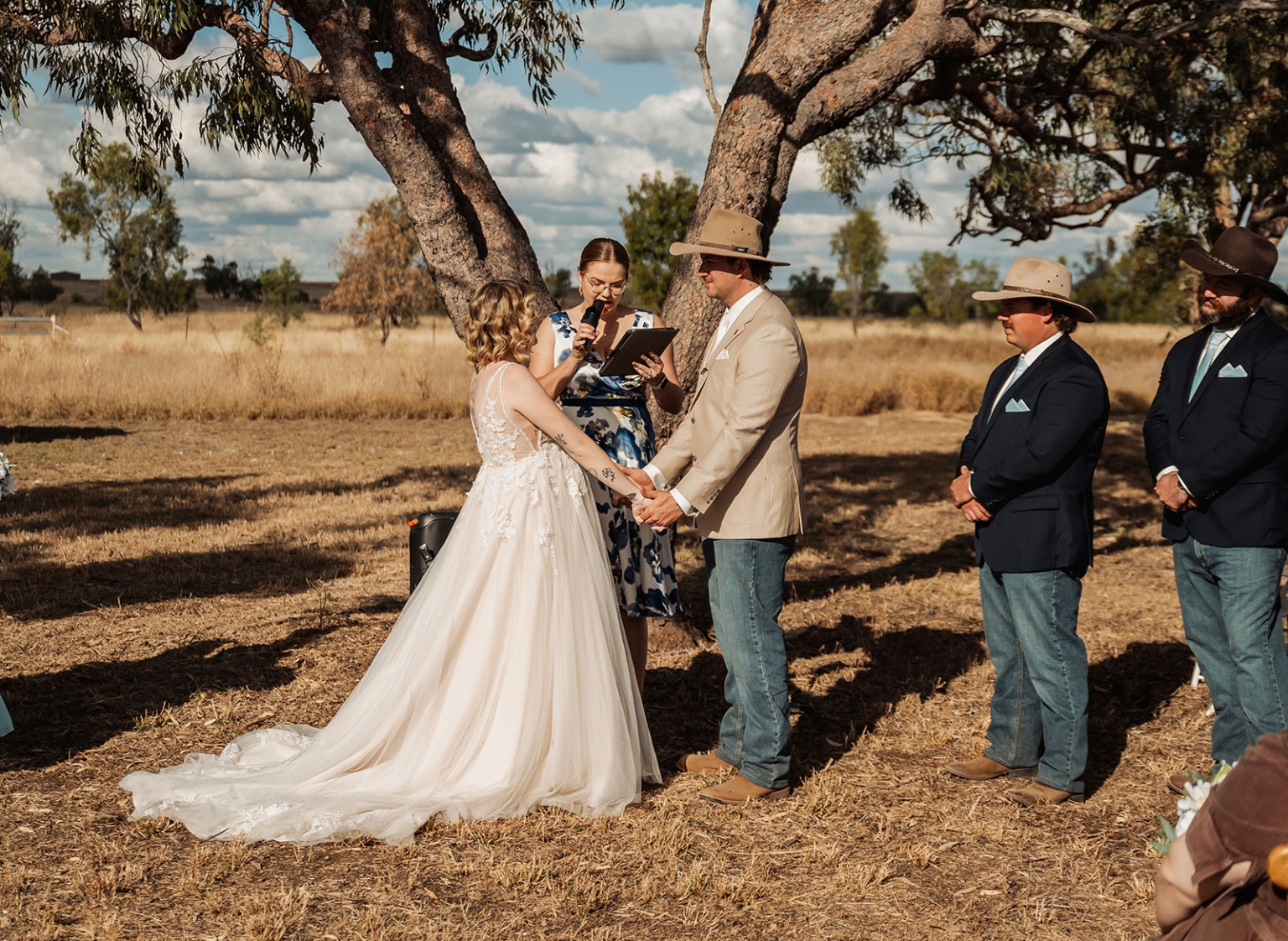 capella wedding photography – caitlin & adam’s farm wedding 142 Bride and groom holding hands during an outdoor farm wedding ceremony beneath gum trees in Capella