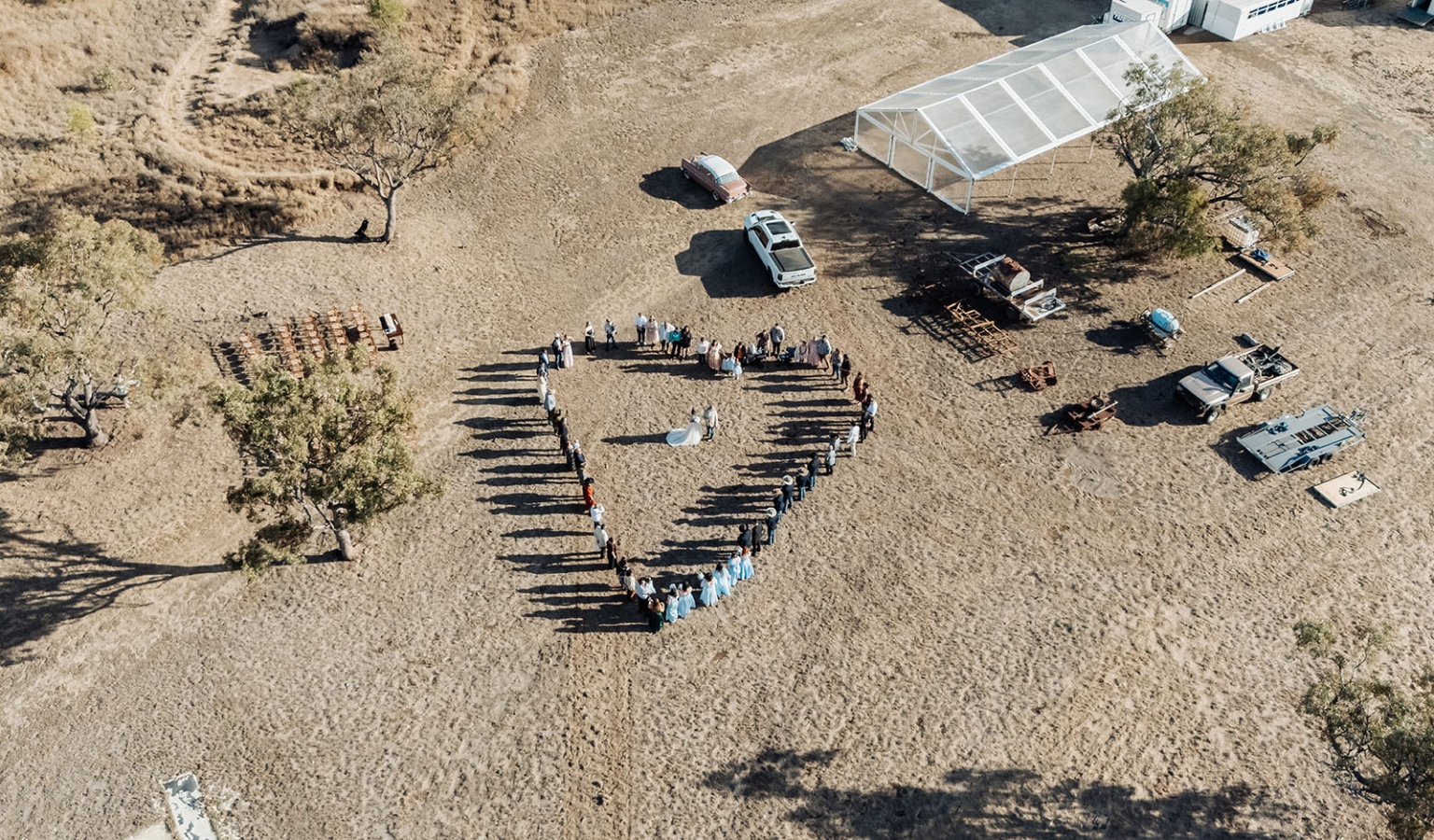 capella wedding photography – caitlin & adam’s farm wedding 150 Aerial view of wedding guests forming a heart around the newlyweds on a dry farm paddock beside a marquee in Capella.