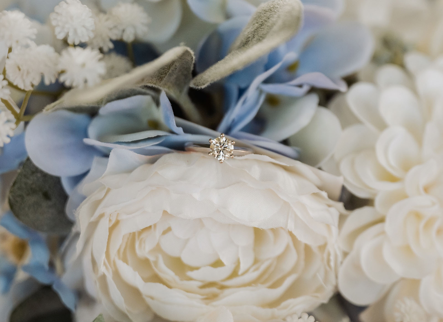 capella wedding photography – caitlin & adam’s farm wedding 121 Diamond engagement ring resting on white and pale blue wedding flowers