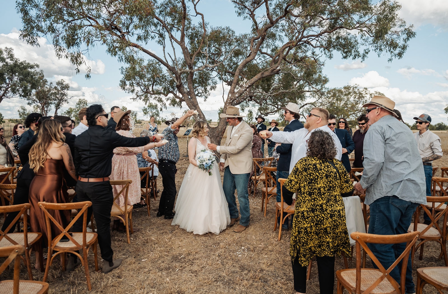 capella wedding photography – caitlin & adam’s farm wedding 149 Newlyweds walk down an outdoor farm wedding aisle as guests throw confetti beneath a large gum tree.