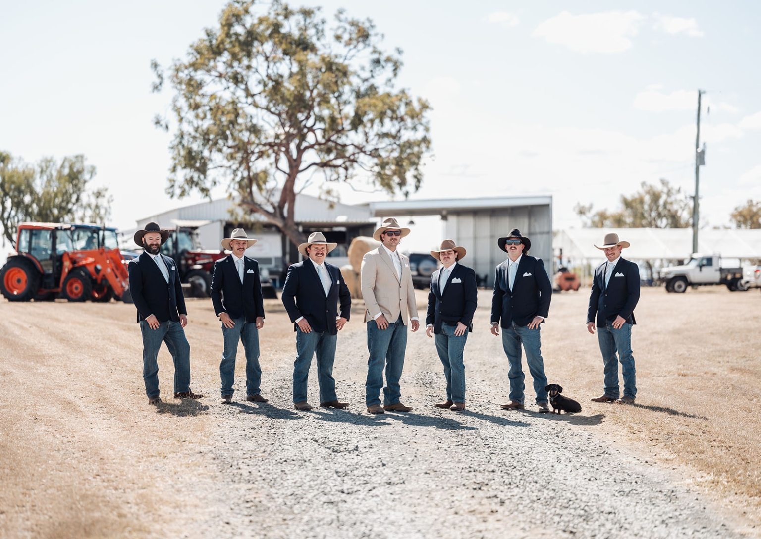 capella wedding photography – caitlin & adam’s farm wedding 119 Groom and six groomsmen in cowboy hats and blazers standing with a small dog on a farm driveway
