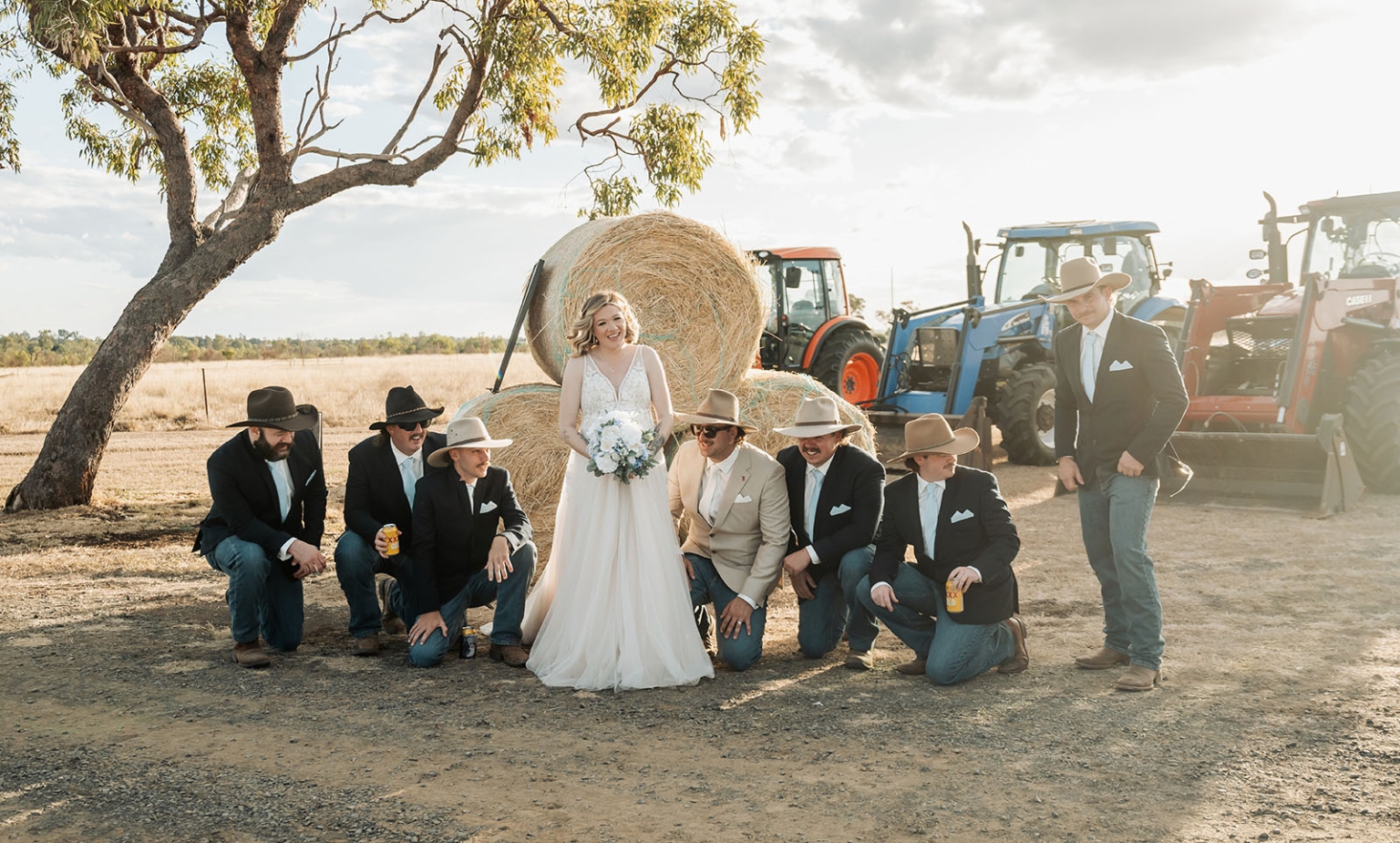 capella wedding photography – caitlin & adam’s farm wedding 155 Bride and groomsmen in cowboy hats pose beside hay bales and tractors at a Capella farm wedding