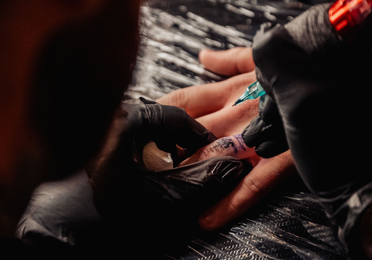 kuitpo hall wedding - courtney & jarrod 261 Tattoo artist creating a detailed finger tattoo with professional machine and black gloves.