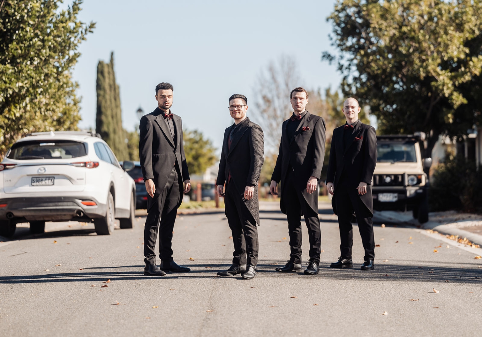 kuitpo hall wedding - courtney & jarrod 196 Four groomsmen in black suits with red accents on suburban street.