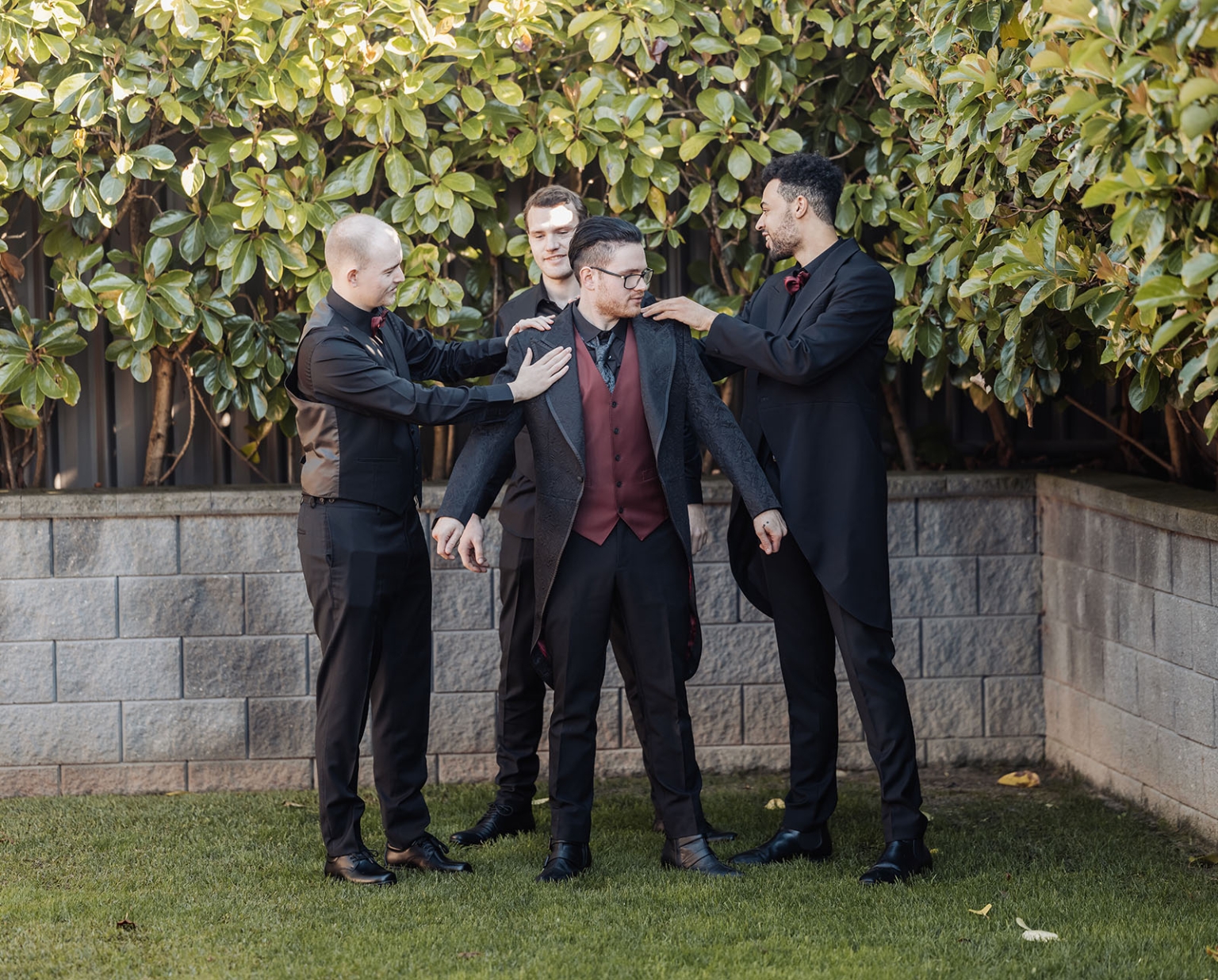 kuitpo hall wedding - courtney & jarrod 197 Wedding party groomsmen adjusting groom’s burgundy formal suit outdoors.