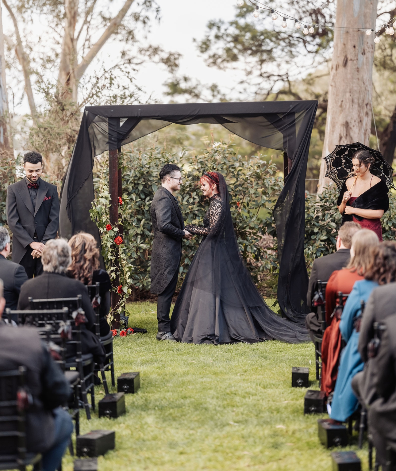kuitpo hall wedding - courtney & jarrod 228 Gothic outdoor wedding ceremony with black-dressed couple under floral wooden arch.