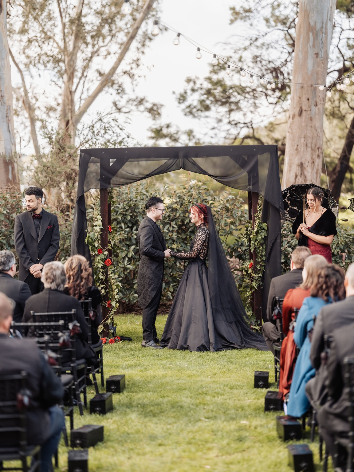 kuitpo hall wedding - courtney & jarrod 226 Gothic outdoor wedding ceremony with black gown, red roses, and woodland arch.