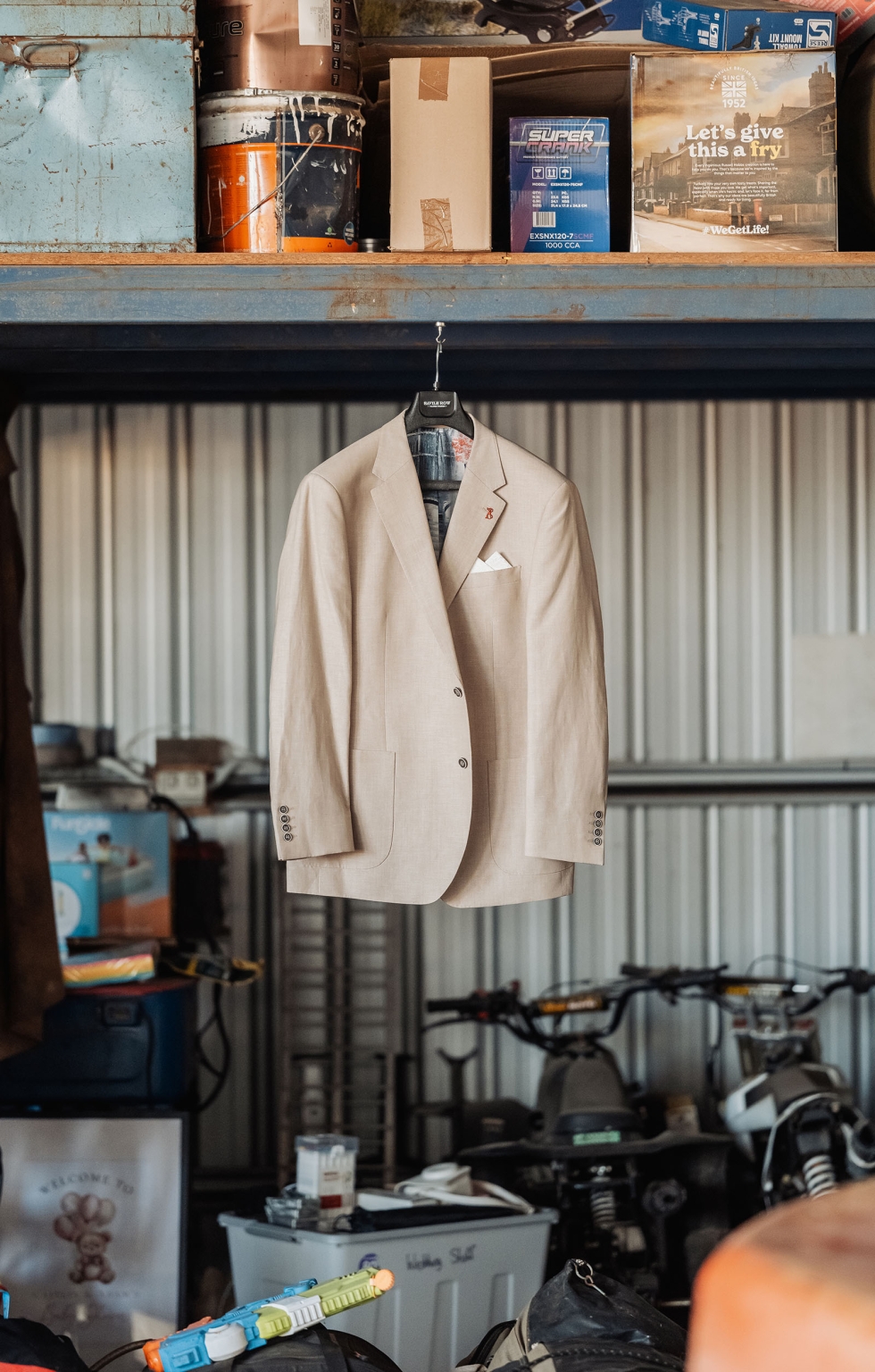 capella wedding photography – caitlin & adam’s farm wedding 112 Beige groom’s suit jacket hanging in a corrugated farm shed beside workshop tools and motorbikes